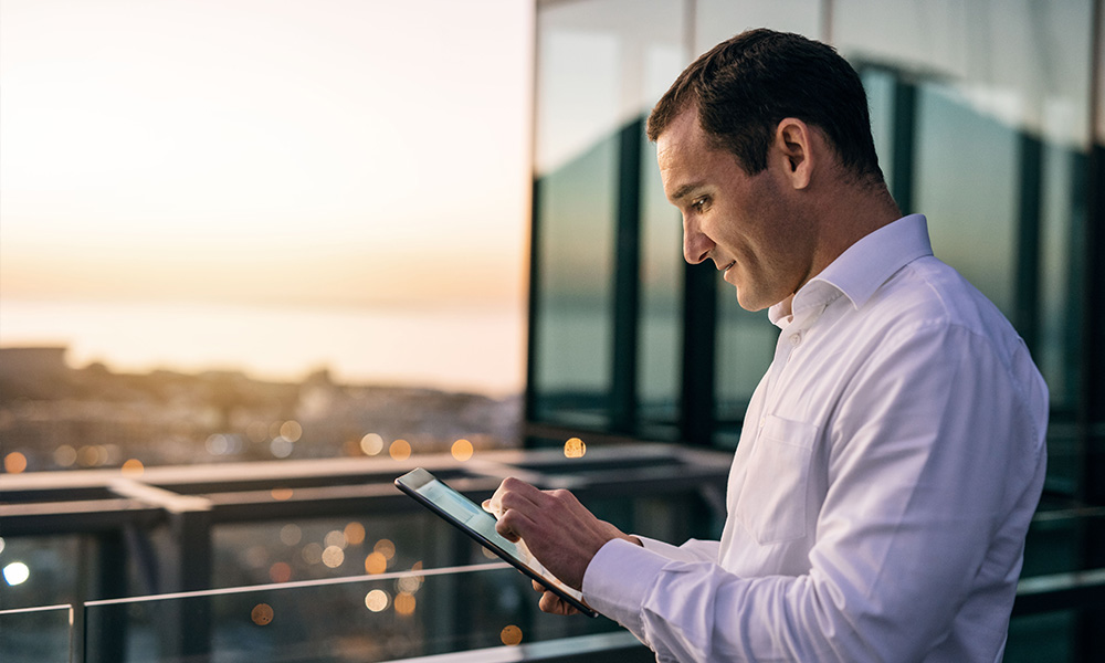 A man stands on a balcony viewing data on a tablet.